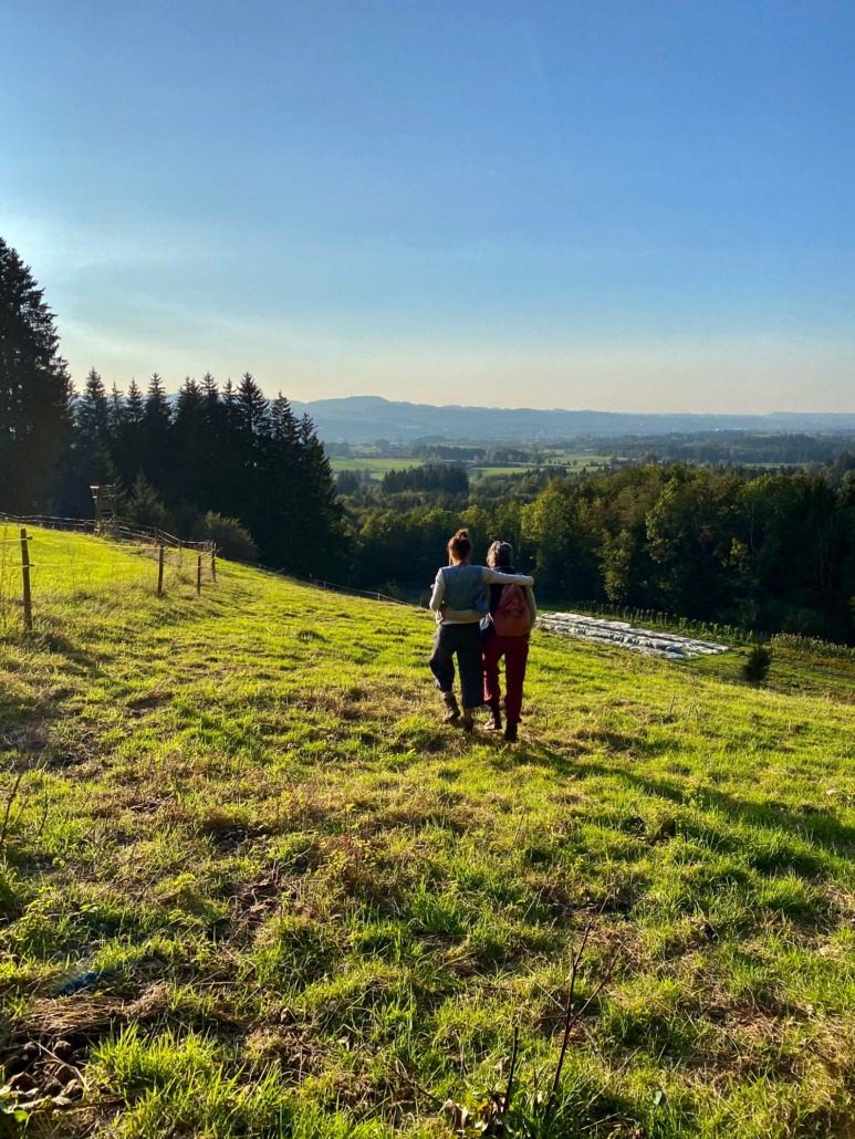 Zwei Menschen gehen über eine Wiese, im Hintergrund eine weite Landschaft